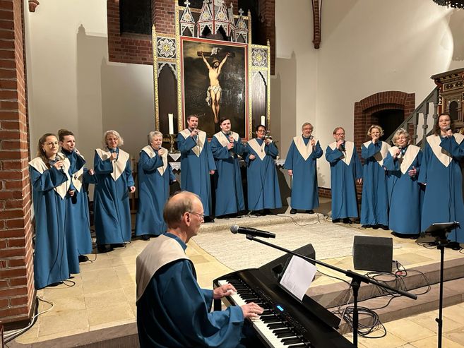 Ein Gospelchor in blauen Roben singt in einer Kirche vor einem Altarbild. Ein Mann spielt Klavier im Vordergrund.