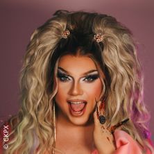 Person mit voluminösem, lockigem Haar und auffälligem Make-up vor rosa Hintergrund.