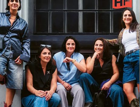 Fünf Frauen sitzen lächelnd auf einer Fensterbank vor einem Gebäude.