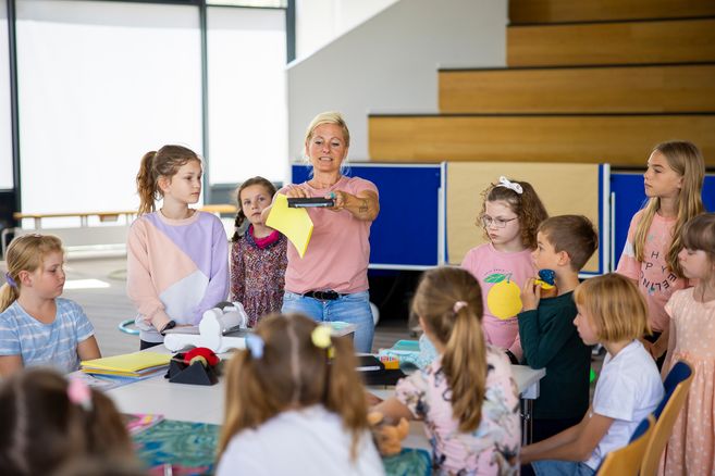 Eine Frau zeigt einer Gruppe von Kindern ein gelbes Blatt Papier in einem Klassenzimmer.