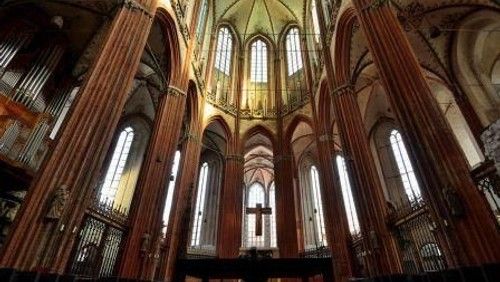Innenansicht einer gotischen Kirche mit hohen Säulen und Buntglasfenstern.