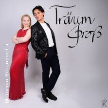 Ein Mann und eine Frau posieren elegant vor einem neutralen Hintergrund mit dem Schriftzug 'Träum groß'.