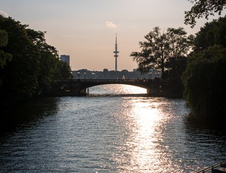 Sonnenuntergang über einem Fluss mit Brücke und Fernsehturm im Hintergrund.