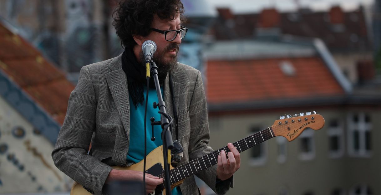 Musiker mit Gitarre auf einem Dachgeschoss vor seinem Mikrofon