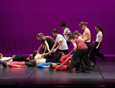 Eine Gruppe von Schülern führt eine Tanzperformance auf einer Bühne mit violettem Hintergrund auf.