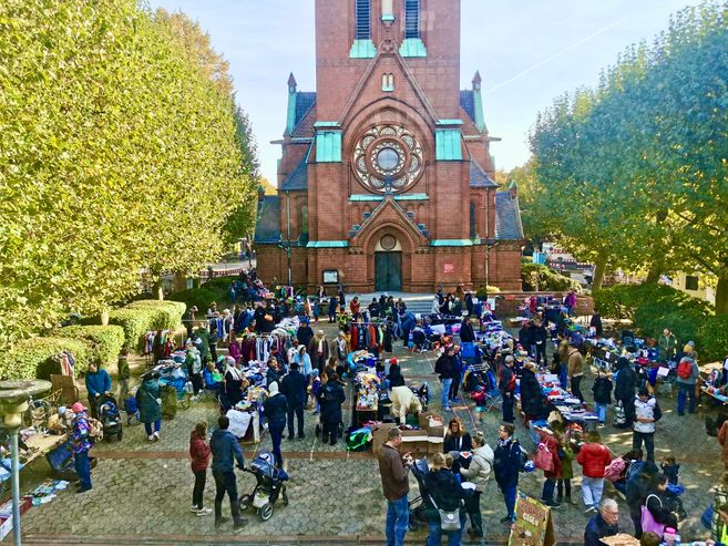 Ein belebter Flohmarkt auf einem Kirchplatz mit vielen Ständen und Besuchern vor einer großen Backsteinkirche.