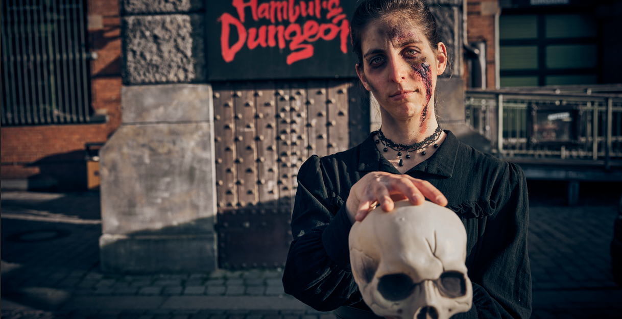 Geschminkte Schauspielerin steht vor dem Hamburg Dungeon Logo