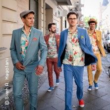 Vier Männer in bunten Anzügen gehen eine Straße entlang.