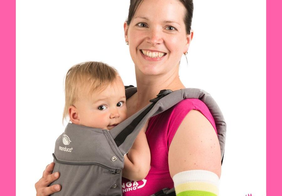 Frau mit Baby in einer Trage, lächelnd, vor weißem Hintergrund mit pinkem Rahmen und Kanga Training Logo.