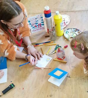 Erwachsene und zwei Kinder basteln an einem Tisch mit Farben und Papier.