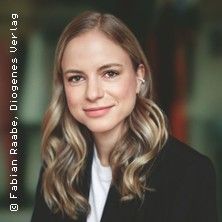 Porträt einer lächelnden Frau mit langen, blonden Haaren in einem schwarzen Blazer.