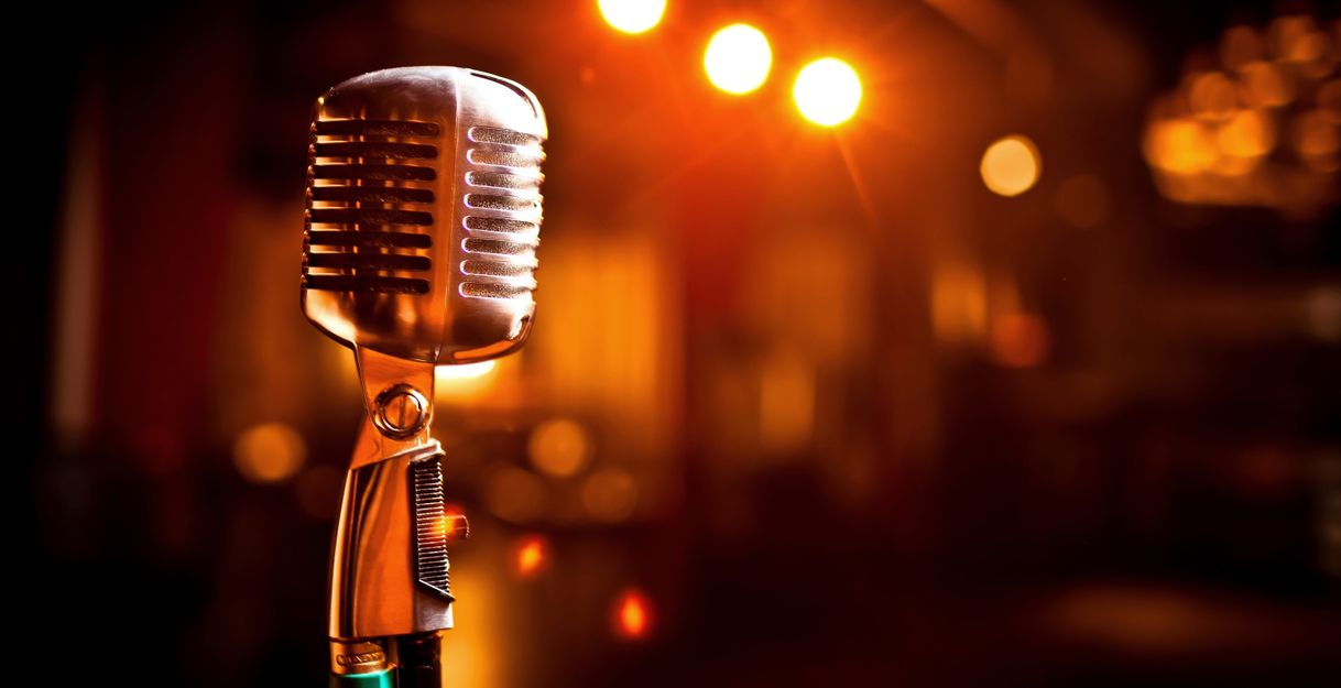 Ein Vintage-Mikrofon im Vordergrund mit unscharfen Lichtern im Hintergrund.