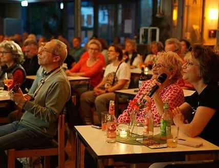Menschen sitzen in einem gemütlichen Raum und singen Karaoke, während sie Getränke genießen.