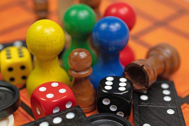 Nahaufnahme von bunten Spielfiguren, Würfeln und Dominosteinen auf einem Spielbrett.