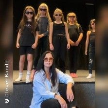 Eine Gruppe von Kindern und eine erwachsene Person posieren auf einer Bühne, alle tragen Sonnenbrillen.
