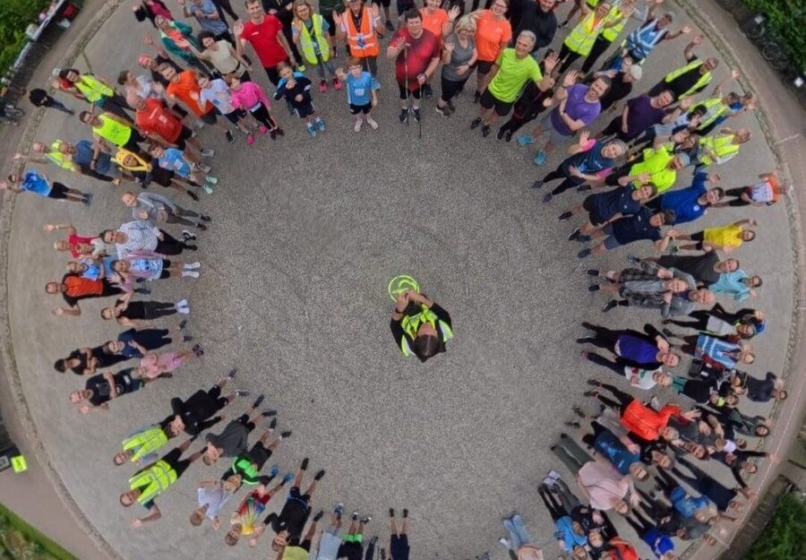 Gruppe von Menschen steht im Kreis auf einem Platz, umgeben von Gebäuden und Bäumen.