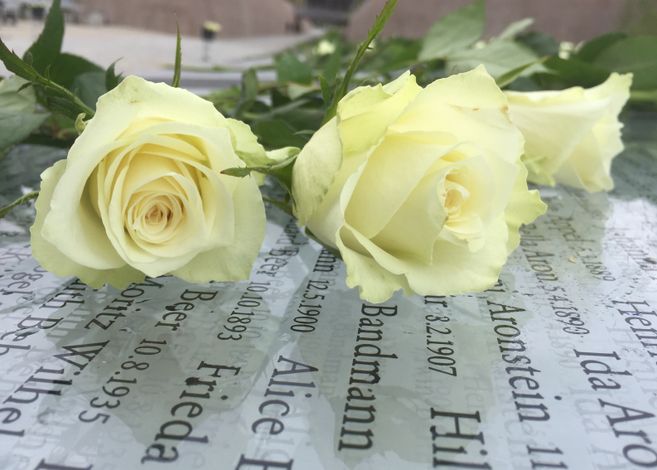 Zwei Blumen auf einer Gedenktafel mit eingravierten Namen