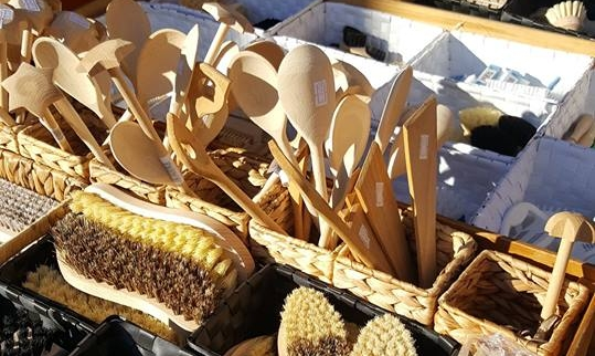 Verschiedene Holzutensilien und Bürsten in Körben auf einem Marktstand.