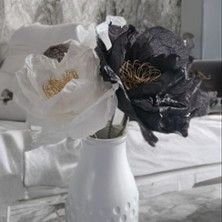 Zwei Papierblumen in Schwarz und Weiß in einer weißen Vase auf einem Tisch.