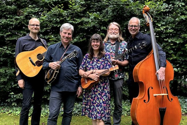 Eine fünfköpfige Band mit verschiedenen Instrumenten posiert vor einer Hecke.