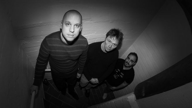 schwarz/weiß foto, drei Männer stehen in einem engen Treppenhaus von oben forografiert