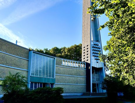 Außenansicht der Dreifaltigkeitskirche mit modernem Turm und Glasfassade, umgeben von Bäumen.