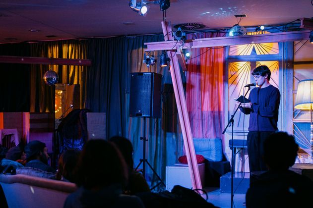 Ein Autor steht auf der Bühne vor Publikum in gemütlichem Setting