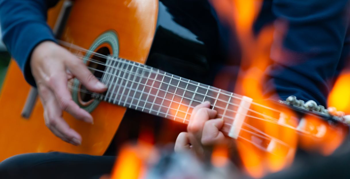 Nahaufnahme einer Person, die Gitarre spielt, mit Flammen im Vordergrund.