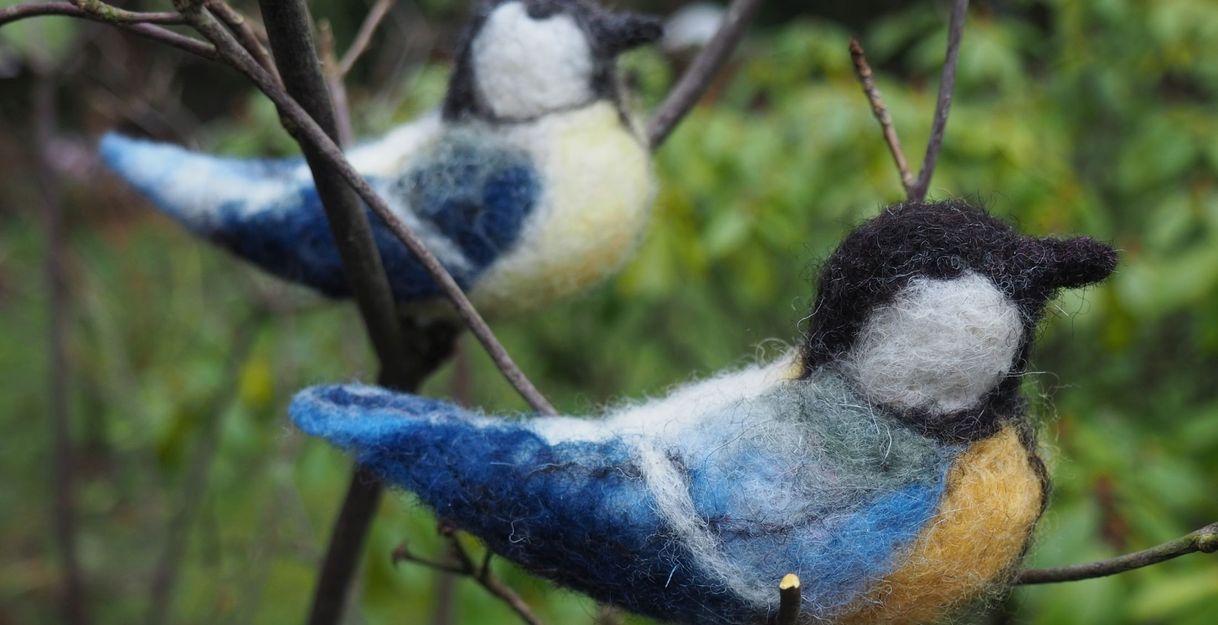 Zwei gefilzte Vögel auf Zweigen im Freien.