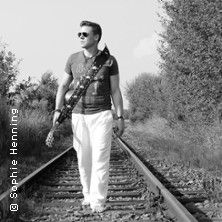 Schwarz-weiß Foto eines Mannes mit Gitarre auf Bahngleisen.