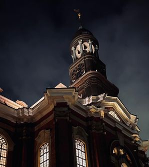 Nachtaufnahme der St. Michaelis Kirche mit beleuchtetem Turm und dunklem Himmel.