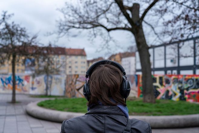 Person mit Kopfhörern steht vor einer mit Graffiti bedeckten Wand in einem urbanen Park.