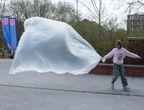 A girl is dragging a huge, thin plastic bubble behind her, filled with a large amount of air.