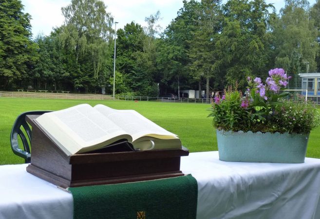 Ein Altar mit einer offenen Bibel und Blumenschmuck auf einem Tisch, der auf einem Fußballfeld steht.