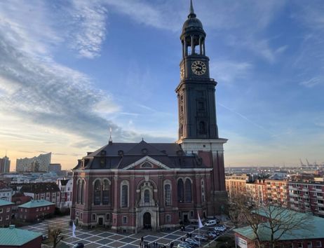 Die Kirche St. Michaelis in Hamburg mit ihrem markanten Turm und der Elbphilharmonie im Hintergrund bei Sonnenuntergang.