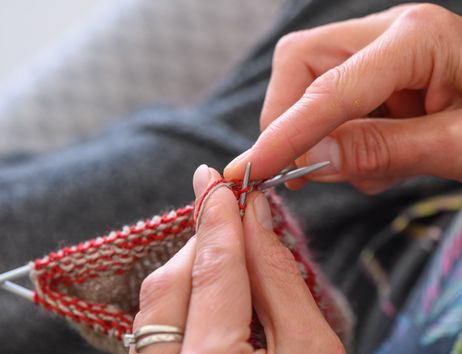 Nahaufnahme von Händen, die mit Stricknadeln und rotem Garn stricken.