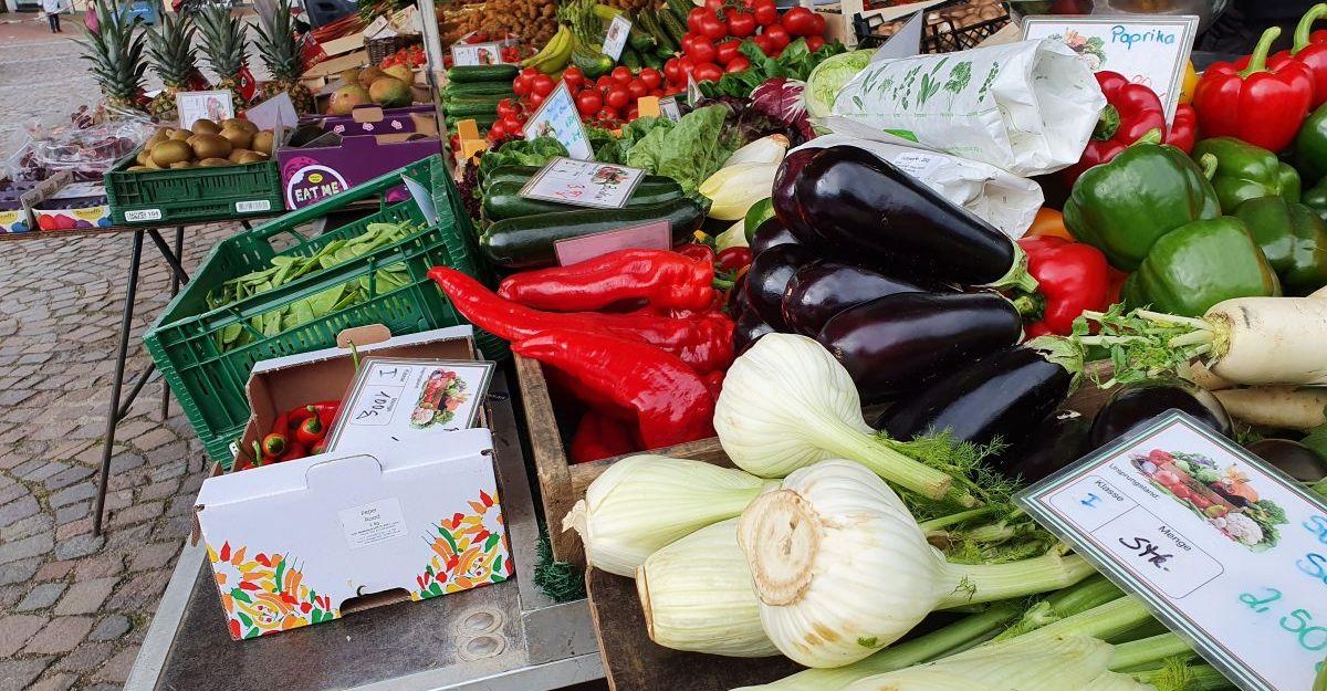Ein Marktstand mit frischem Gemüse wie Paprika, Auberginen und Fenchel auf einem Wochenmarkt.