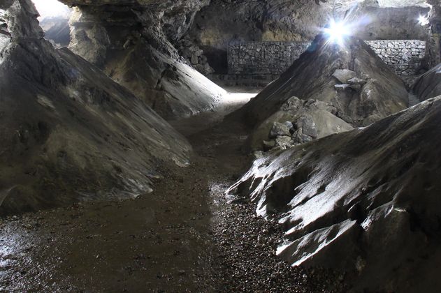 Innenansicht einer beleuchteten Kalkberghöhle mit steinigen Wänden und Boden.