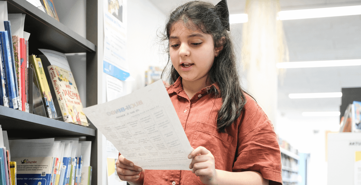 Ein Mädchen liest ein Blatt Papier in einer Bibliothek.