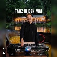 Ein DJ steht vor einem Mischpult, im Hintergrund ein beleuchtetes Gebäude am Wasser. Oben steht 'Tanz in den Mai'.