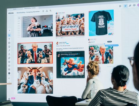 Personen betrachten eine Präsentation mit Memes und Bildern auf einem großen Bildschirm.