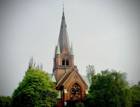 Eine gotische Kirche mit einem hohen Turm und einer Uhr, umgeben von Bäumen.