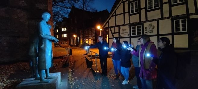 Eine Gruppe von Menschen mit Taschenlampen betrachtet eine Statue in einer historischen Stadt bei Nacht.