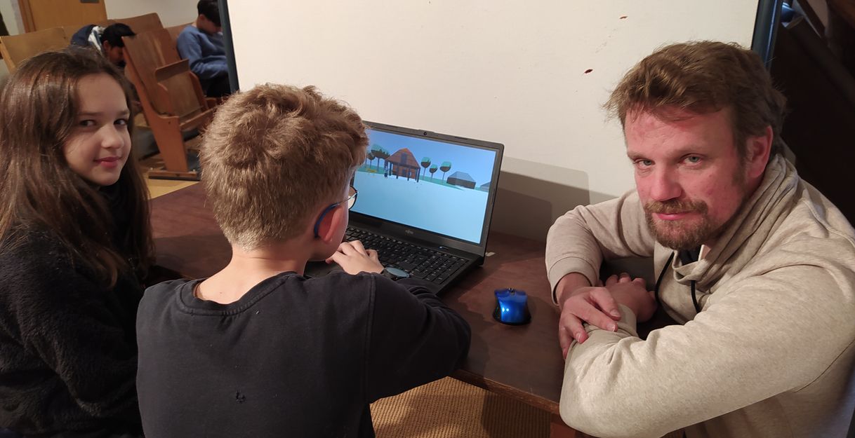 Ein Mann und zwei Kinder sitzen an einem Tisch mit einem Laptop, auf dem ein digitales Modell angezeigt wird.