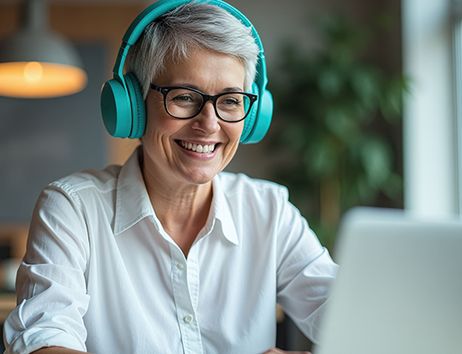 Man sieht eine Frau mit türkusblauen Kopfhörern vor einem Laptop Bildschirm