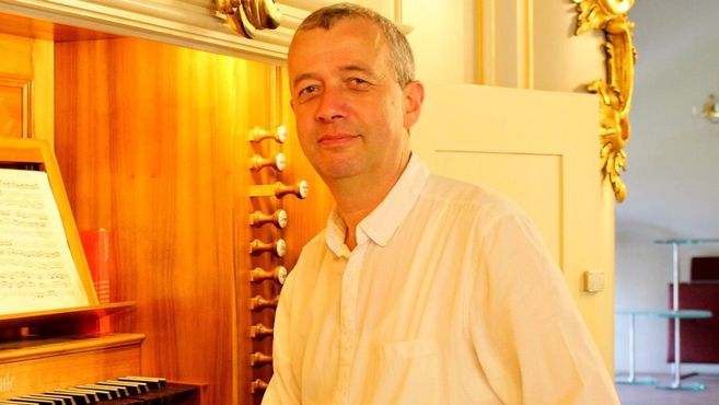 Ein Mann steht vor einer Orgel in einem hellen Raum.