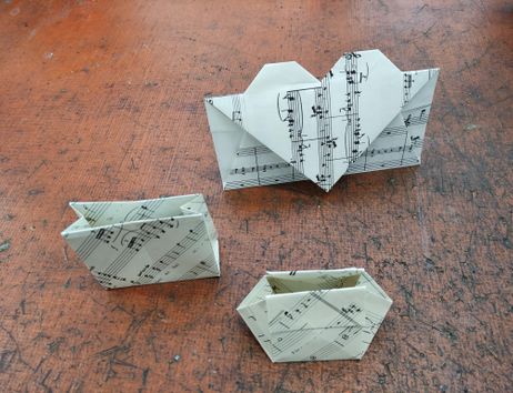 3 gefaltete Objekte aus Notenpapier. Zwei Taschen und ein Briefumschlag mit einem gefaltetem Herz.