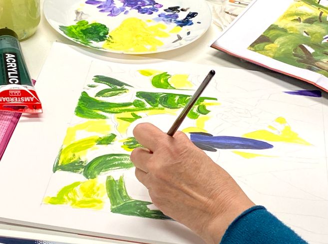 Eine Person malt die ersten Pinselstriche eines helles Bildes mit Acrylfarben in grün und violett