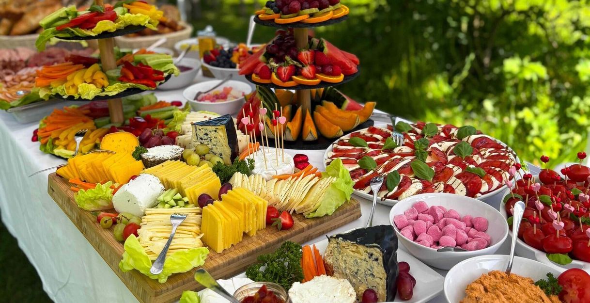 Ein reichhaltiges Buffet mit Käse, Obst, Gemüse und verschiedenen Dips auf einem Tisch im Freien.