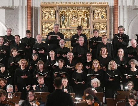 Ein Chor singt in einer Kirche vor einem kunstvollen Altar.